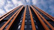 © Evgenii - Tall residential structure showcases a unique orange facade against a backdrop of blue and gray clouds, highlighting contemporary architecture in an urban setting