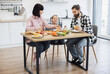 © sofiko14 - Caucasian family with parents and young daughter enjoying breakfast with pizza, fruit, and salad at home kitchen table. Warm family bonding and morning routine.