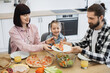 © sofiko14 - Caucasian family with parents and daughter enjoying pizza breakfast at home. Happy bonding moment around kitchen table with salad and juice.