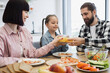 © sofiko14 - Happy Caucasian family with young parents and daughter clinking glasses of juice during breakfast in bright kitchen. Fresh fruits and healthy food create joyful atmosphere.