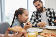 © sofiko14 - Caucasian family with young daughter having breakfast together enjoying pizza. Happy morning moment shared at home, capturing warmth of family bond.