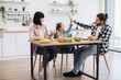 © sofiko14 - Caucasian family enjoying breakfast together. Young daughter gives high five to dad, creating joyful moment. Mother smiles, observing interaction. Healthy breakfast includes fruits and vegetables.