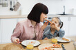 © sofiko14 - Caucasian mother and young daughter sitting together enjoying pizza for breakfast at home. Warm family moment with orange juice and smiling faces.