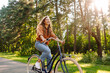 © maxbelchenko - Happy woman riding bicycle bike on sidewalk in city green park outdoors. Active lifestyle concept.