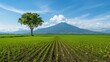 © Kunalai - precision farming concept Lush green field with a lone tree and a mountain backdrop under a blue sky.