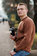 © Galka3250 - Young Man in Brown Sweatshirt Holding Coffee Cup in Park Setting