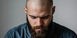 © StockKing - Serious young bearded man with a bald head looking down thoughtfully against a soft gray backdrop emphasizing introspection and calmness.