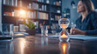 © Rachakrit - Hourglass on desk symbolizes time management in modern office setting, with focused woman in background