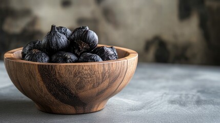 Poster - Close up of black garlic cloves in a wooden bowl on a textured surface with empty space for culinary or health related text