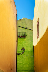 Wall Mural - Colorful yellow and green walls with a streetlamp in a street in the old mediterranean village of Bosa, Sardinia island, Italy