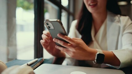 Aufkleber - Young businesswoman is using smartphone while sitting in cafe near window, she is wearing white shirt and blazer, smartwatch, notebook and pen are on table