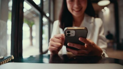 Poster - Young businesswoman sitting at cafe table. Engaging with smartphone. Radiating professional energy while working remotely. Digital device complementing elegant workspace with notebook and pen nearby