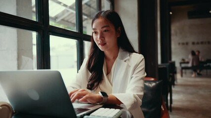 Aufkleber - Professional asian businesswoman working diligently on her laptop near large window inside modern, bright cafe environment, embodying digital nomad lifestyle with focused concentration