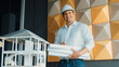 © Summit Art Creations - Portrait of professional project manager holding project plan with house model at table. Professional architect engineer wearing safety helmet while standing posing with confident. Manipulator.