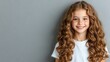 © pvl0707 - Young girl with long curly hair smiles brightly against a grey background in a cheerful indoor setting during the afternoon