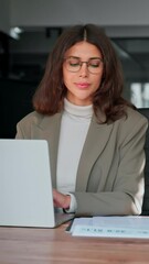 Wall Mural - Focused latin hispanic young business woman working on laptop computer reading financial document report in office. Accountant entrepreneur manager businesswoman doing paperwork using pc. Vertical