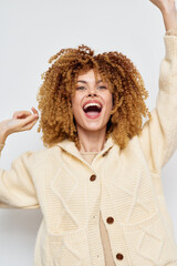 Wall Mural - Happy woman with curly hair celebrating joyfully wearing a cozy knitted sweater against a light background, showcasing vibrant and positive emotions