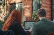© Mediaphotos - Two people sitting outdoors using laptop, analyzing data on screen. Brick walls and large windows in background add to the professional setting