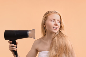 Wall Mural - Beautiful young woman drying her hair with hairdryer on beige background