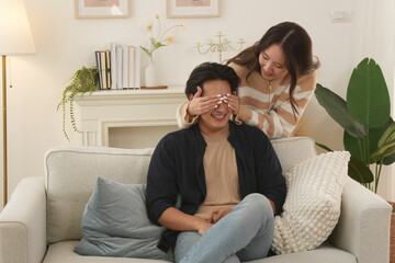 Asian family happy and warm love girlfriend standing on sofa blindfolded handsome husband sitting on sofa happy romantic together in living room at home