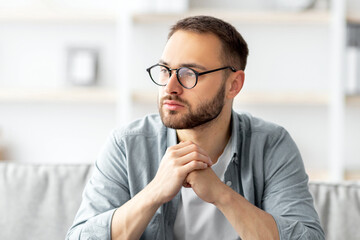 Poster - Serious young Caucasian guy sitting on couch in front of laptop computer at home. Thoughtful millennial man daydreaming while working online, using portable pc indoors