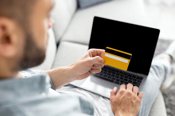 Poster - Contactless shopping, internet banking concept. Unrecognizable young man showing credit card, using laptop, buying goods online, making remote payment at home, mockup for design