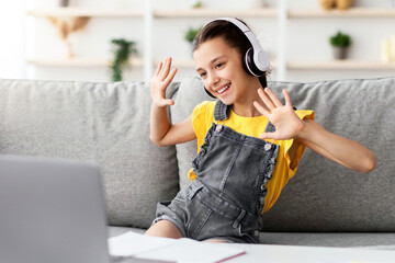 Poster - Distance Education. Portrait of smiling schoolgirl making video call with teacher and classmates, using pc. Cheerful pupil in wireless headphones talking and waving both hands showing ten 10 fingers