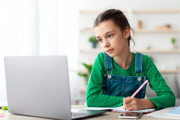 Poster - Web-based Distance Education Concept. Portrait of diligent teen sitting at table in living room, using looking at laptop screen writing in her notebook. Schoolgirl watching online course, taking notes