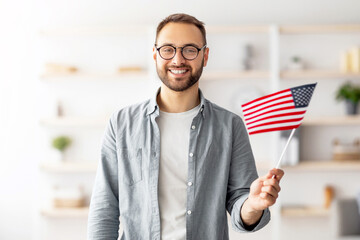 Poster - Handsome young guy holding American flag and smiling at camera indoors. Cheerful millennial man recommending English language school, emigrating to United States. Abroad education and student exchange