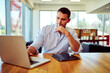 © oscargutzo - Businessman concentrating and thinking while working on laptop in modern office, with tablet on wooden desk