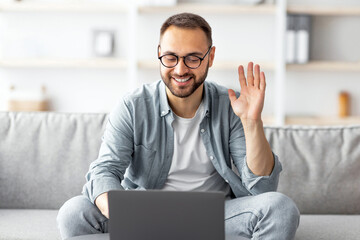 Poster - Online meeting. Happy young Caucasian man using laptop, having video call or business conference, waving at webcam indoors. Millennial guy communicating to colleagues remotely from home office