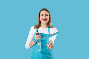 Wall Mural - Young woman with bottle of detergent and squeegee on blue background