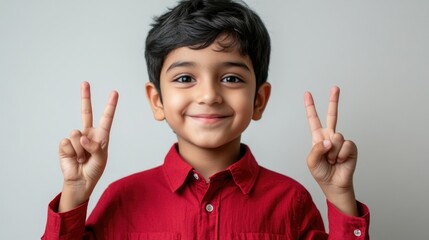 Wall Mural - Cheerful young boy wearing a bright red button-up shirt making peace signs with both hands against a light neutral background