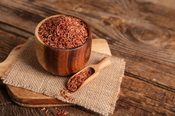 Wall Mural - Board with bowl and scoop of raw brown rice on wooden background