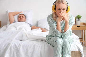 Wall Mural - Mature woman with hearing protectors suffering from her husband's snoring in bedroom