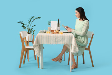 Wall Mural - Young woman at restaurant table on blue background