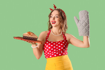 Wall Mural - Young pin-up housewife with oven glove and bun on green background