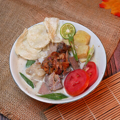 Wall Mural - Soup or Soto Betawi with savory coconut milk broth filled with pieces of potato and beef is a traditional Indonesian food typical of Jakarta. Served in a white bowl on bamboo mat and burlap