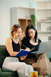 © laddawan - Two women collaborating on a project at home, brainstorming with a laptop and notebook in a cozy setting.