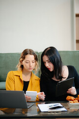 Two women collaborating on a project at home, brainstorming with a laptop and notebook in a cozy setting.