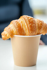 Wall Mural - A croissant is sitting in a paper cup