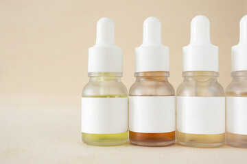 Bottles of facial serum skincare cosmetic products arranged in line on beige background, close-up minimalist mockup