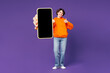 © ViDi Studio - Full body young smiling happy woman wear orange hoody casual clothes hold in hand use close up mobile cell phone show thumb up isolated on plain purple background studio portrait. Lifestyle concept.