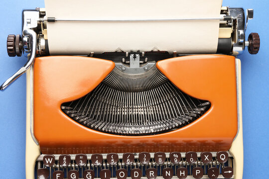 Vintage typewriter with sheet of paper on blue background, top view