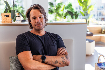 Wall Mural - A confident man with a black shirt and a watch is sitting with his arms crossed