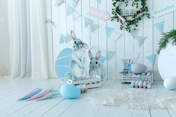 Wall Mural - Baskets with lot colorful Easter eggs and carrots! Holiday flags and festive wreath on white wall. Child room in the spring style. Colorful Easter room interior design with decorative figurine bunny. 