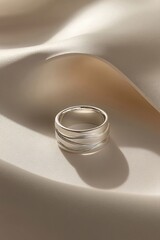 Poster - Silver ring with wave pattern on soft white fabric with subtle shadows and light creating a gentle scene