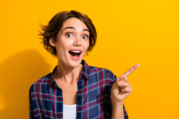 Poster - Portrait of ecstatic nice girl wear checkered shirt indicating at impressive promo empty space isolated on yellow color background