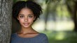 © imagineRbc - A young girl stands calmly next to a tree, showcasing her beautiful curly hair and soft smile. The blurred background creates a peaceful atmosphere during late afternoon light