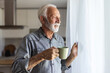 © Jelena Stanojkovic - Senior man drinking coffee and looking thoughtfully out of a window. Old man feel happy drinking coffee in the morning, enjoying time in his home indoor background - lifestyle senior happiness concept